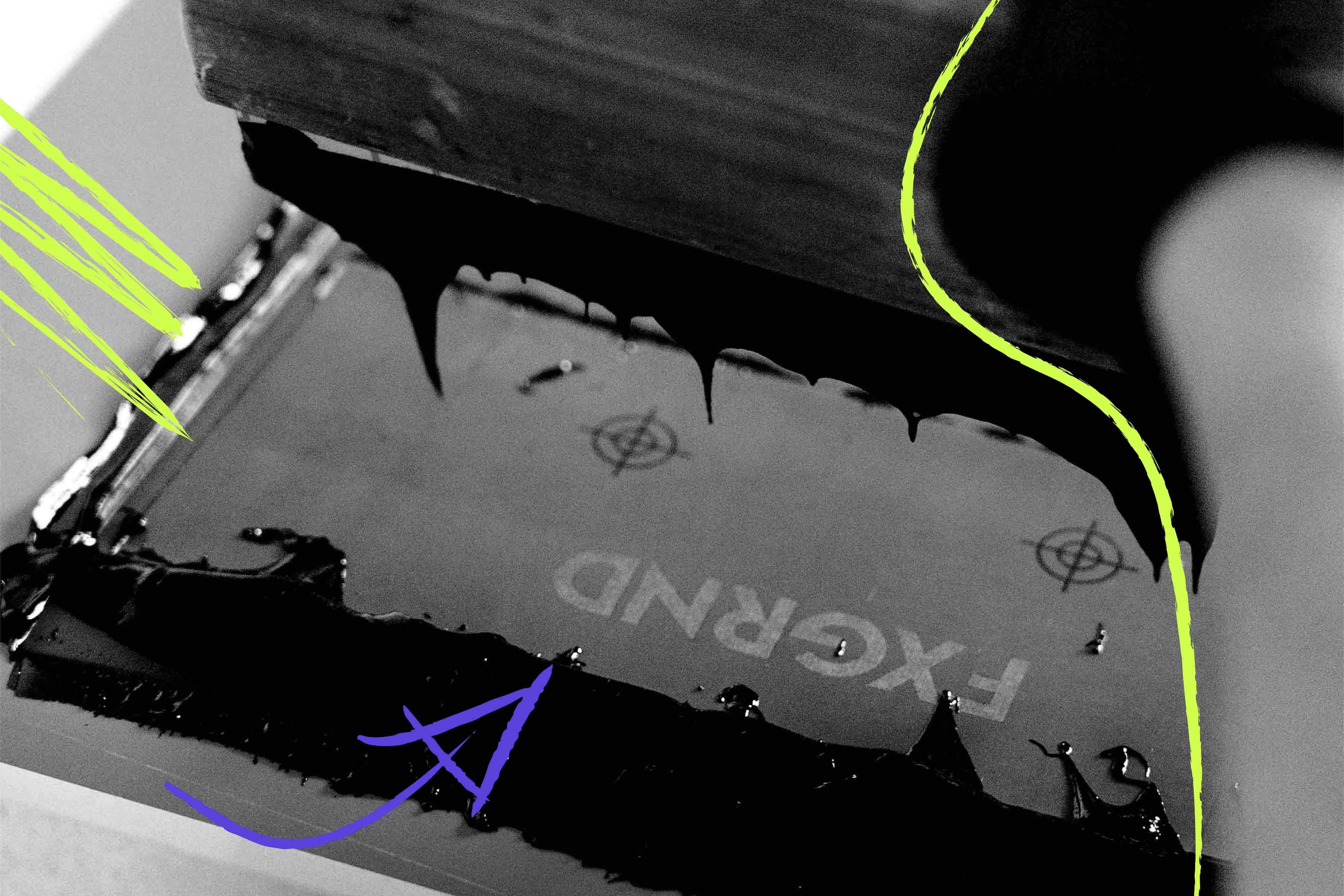 Nahaufnahme eines Siebdruckrahmens mit schwarzer, verlaufender Druckfarbe; das spiegelverkehrte Logo „FXGRND“ ist auf dem Sieb sichtbar, daneben handgezeichnete Markierungen und Pfeile