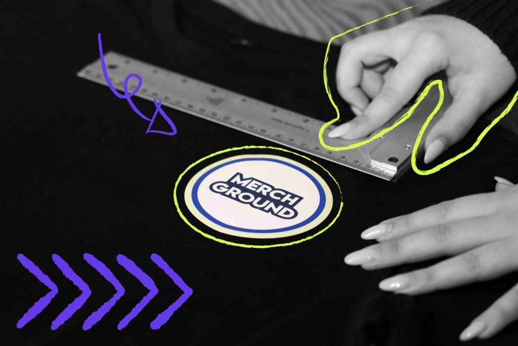 Hände messen mit einem Lineal die genaue Position eines runden Merch-Logos auf einem schwarzen T-Shirt