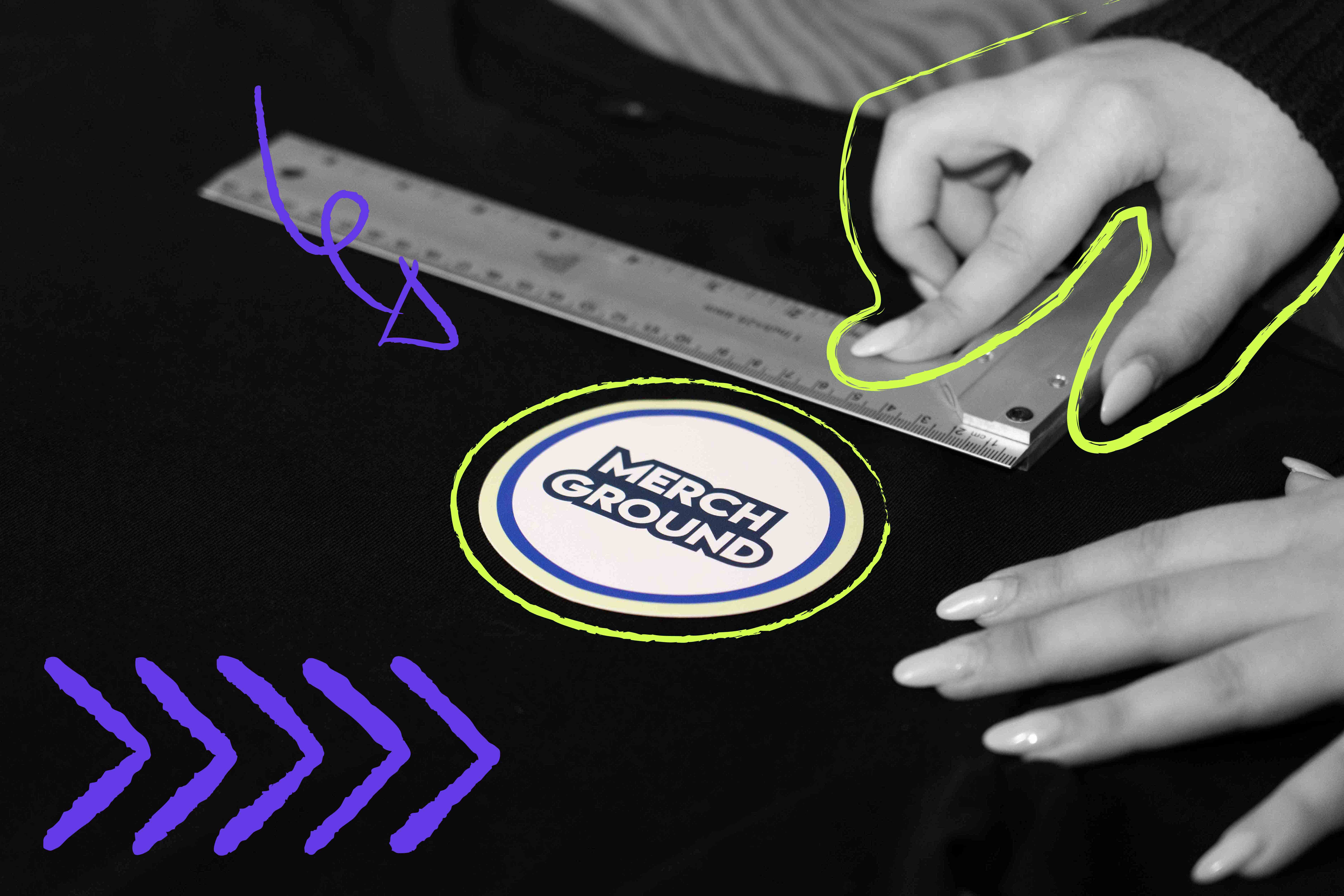 Hände messen mit einem Lineal die genaue Position eines runden Merch-Logos auf einem schwarzen T-Shirt